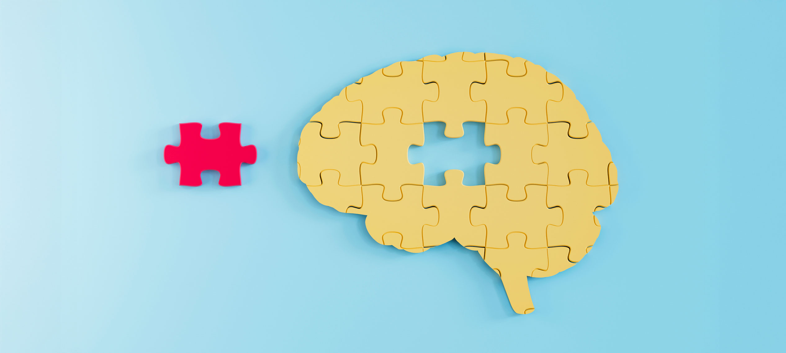 A yellow jigsaw puzzle in the shape of a brain, with one missing piece. The missing piece is red and sits beside the puzzle.
