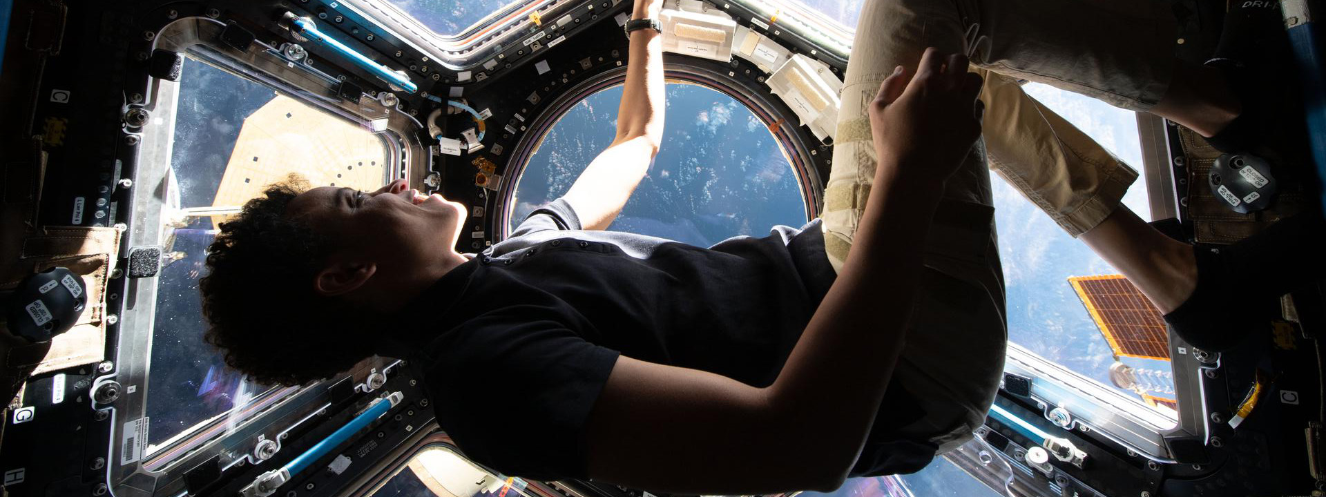 Jessica Watkins floats in the cupola of the International Space Station wearing a blue shirt and khakis