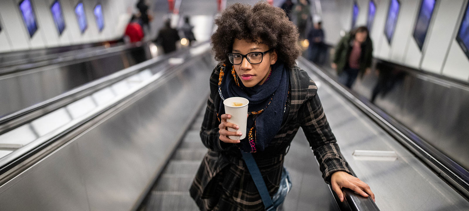 Young woman holding a coffee going up the escalator