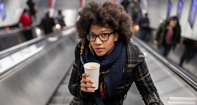 Young woman holding a coffee going up the escalator