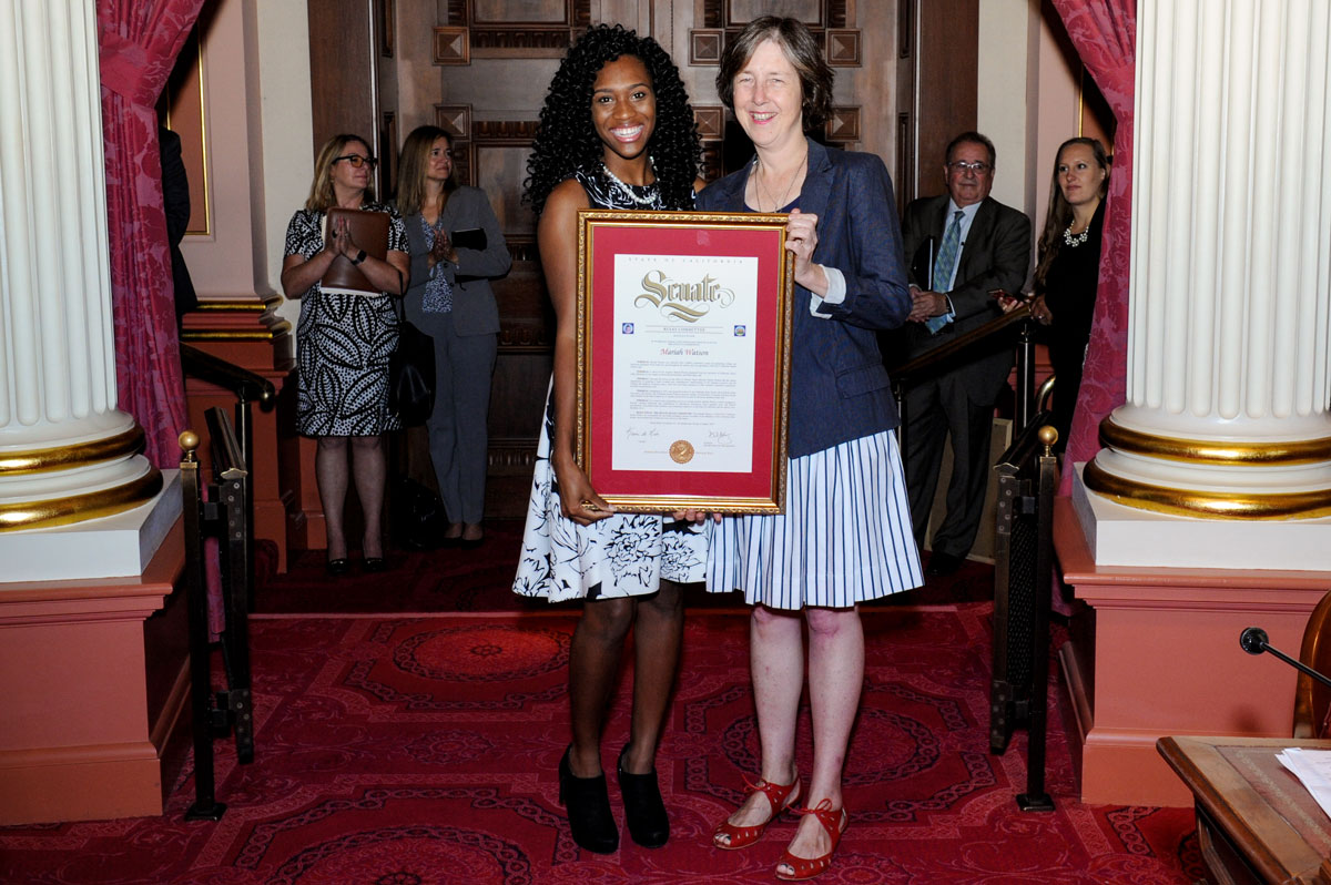 Mariah Watson holds a commemorative plaque for her service in the state Senate next to Sen. Nancy Skinner