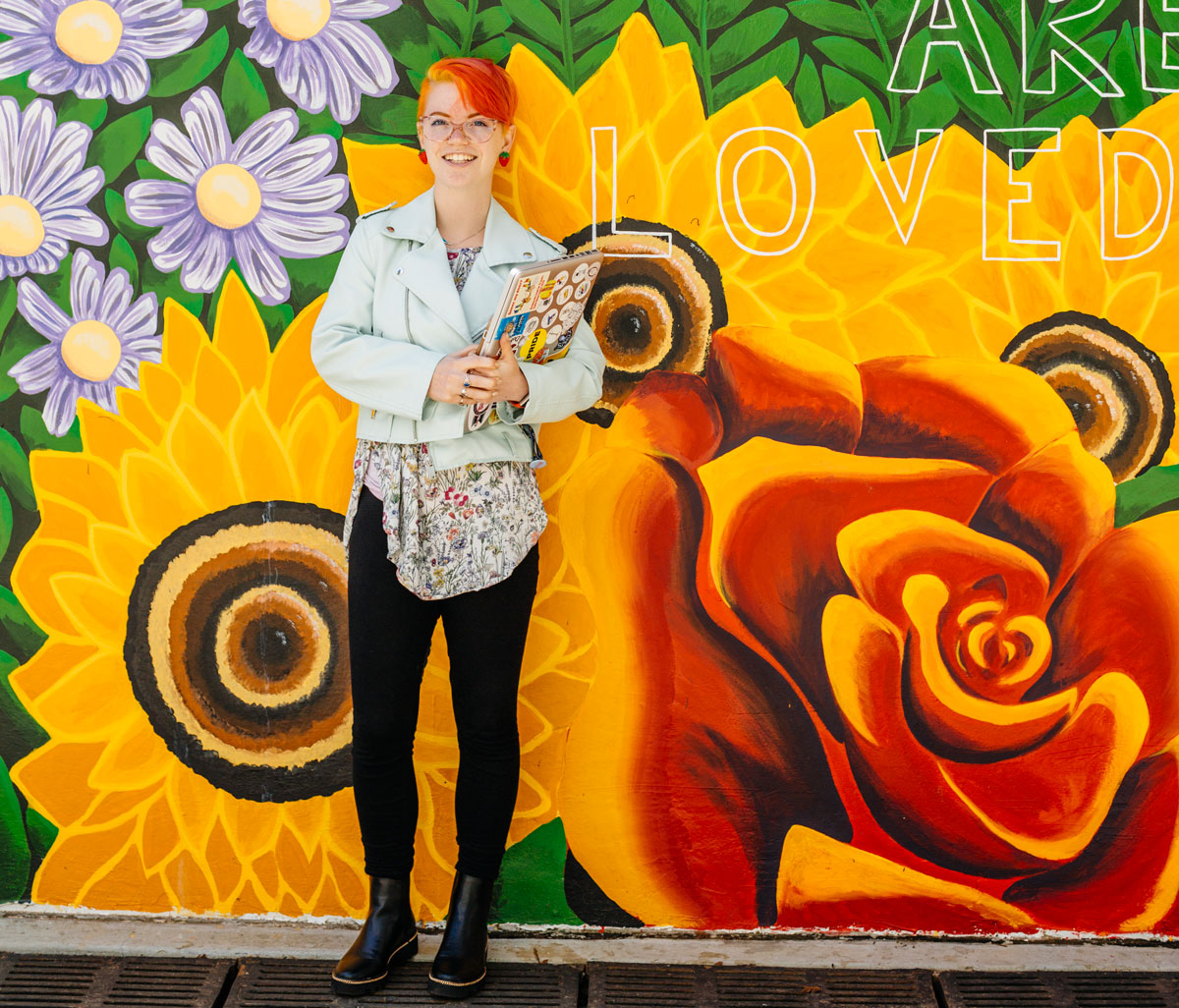 Female student stands in front of colorful red yellow and orange mural