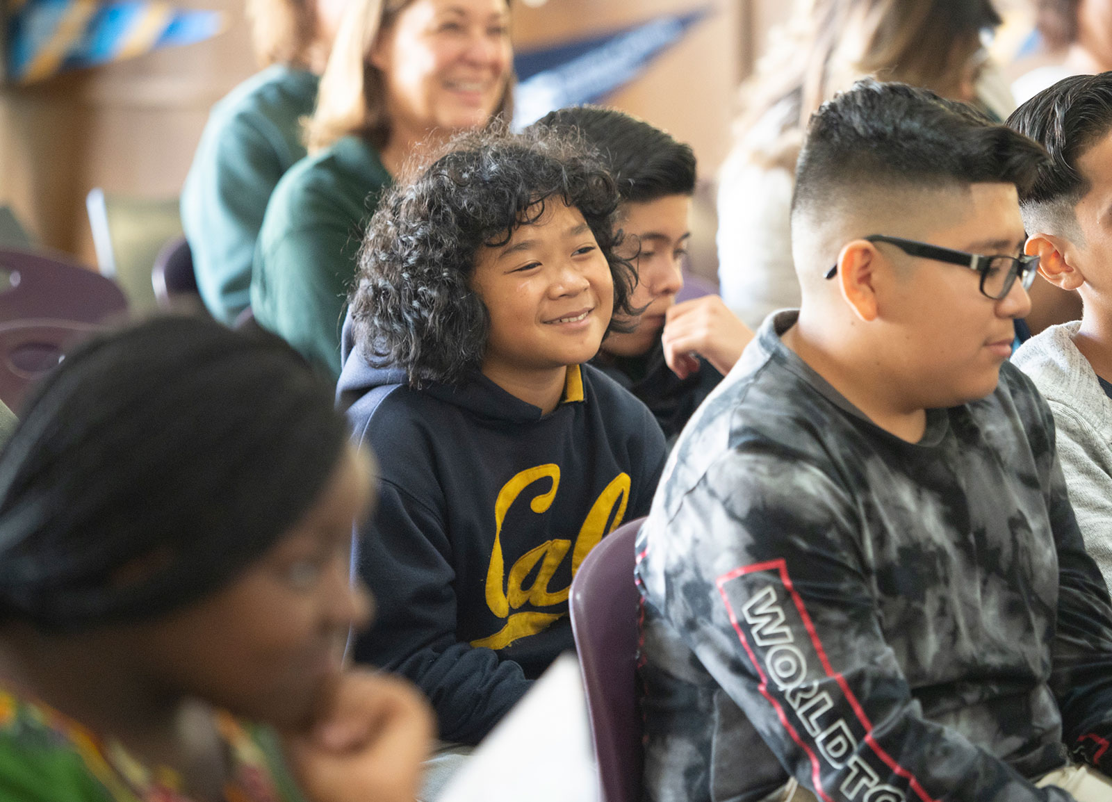 A middle school student listens to a college talk wearing a Cal sweatshirt