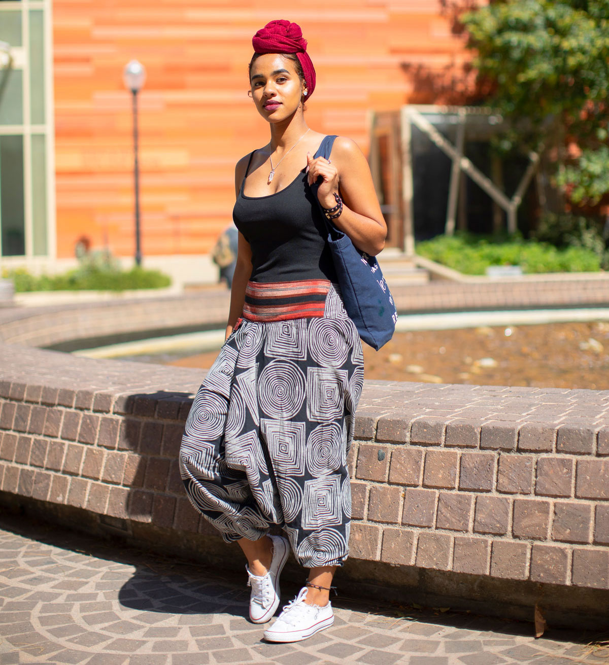 Female student with puffy pants rests against brick