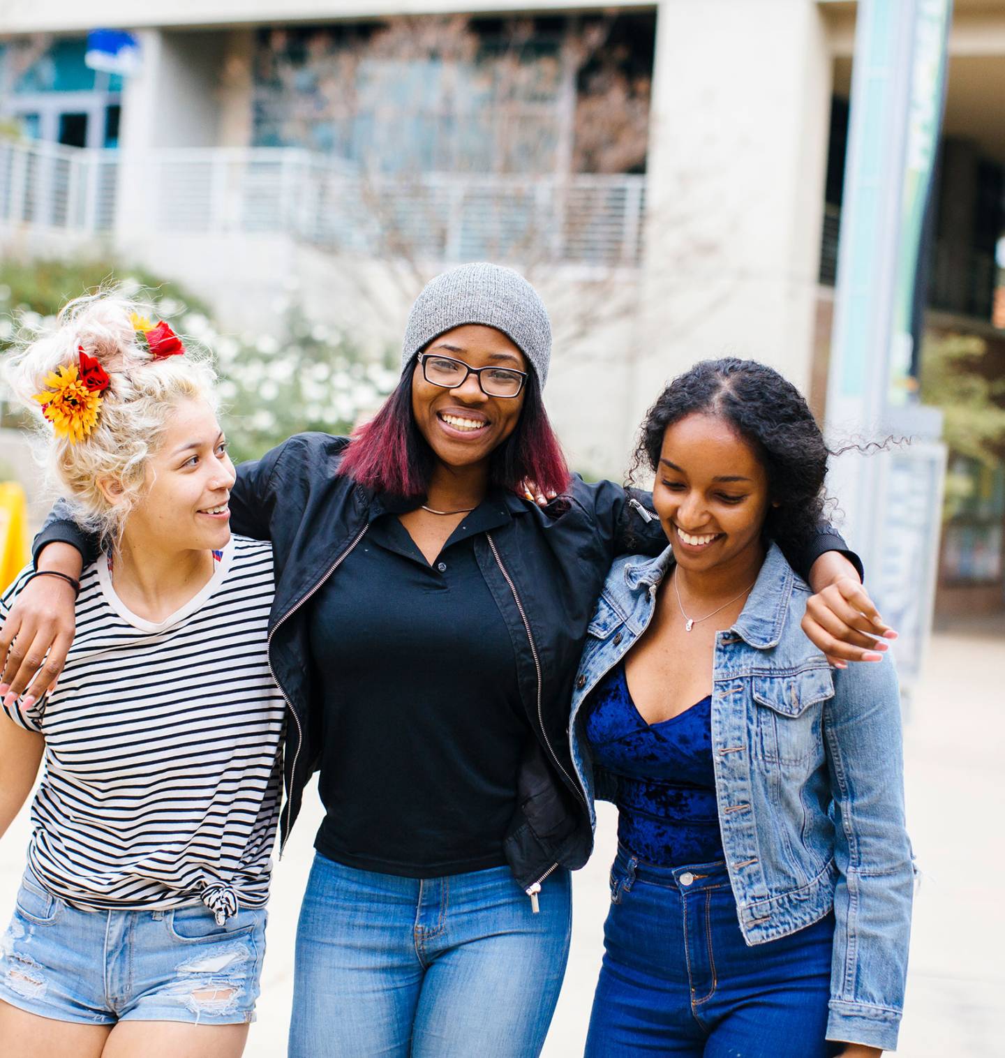 Three students walking together, arms linked on shoulders, on campus