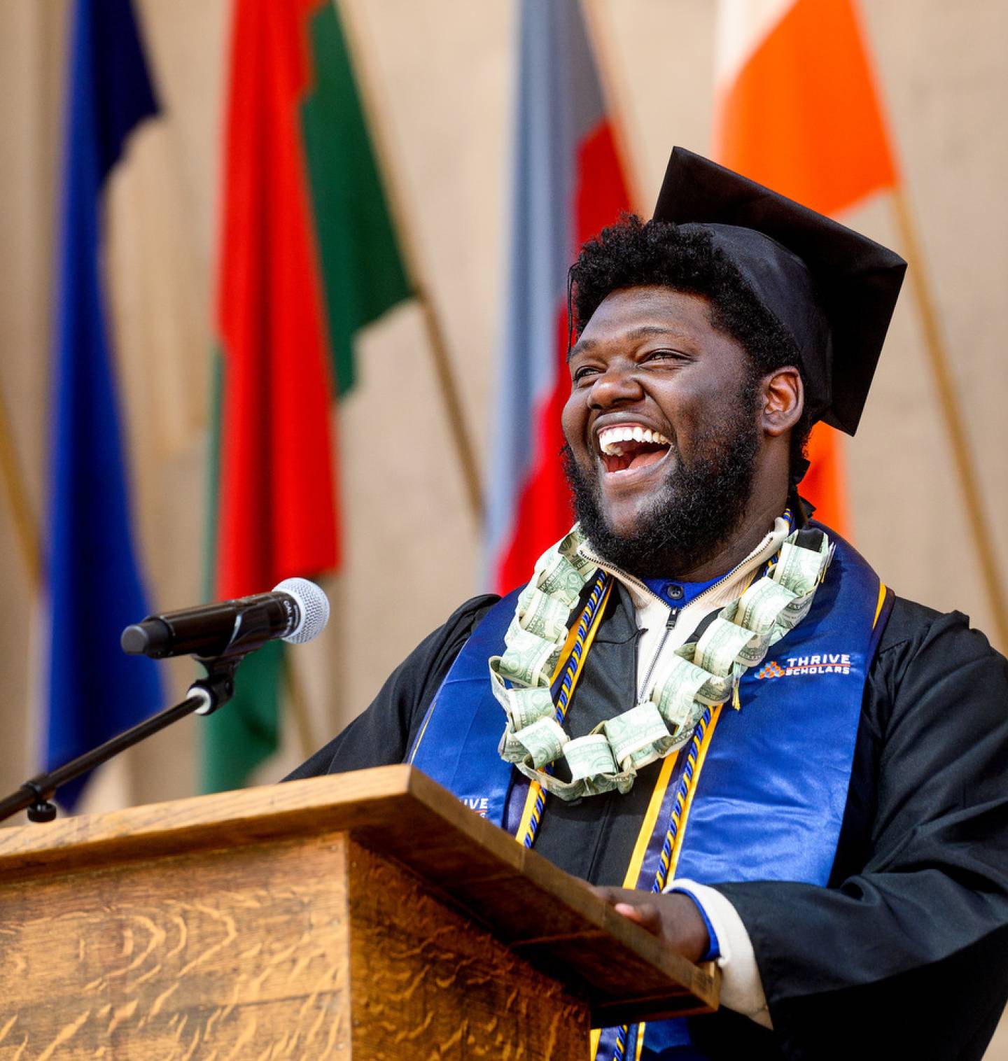 Young male Black graduate laughing while speaking at the podium