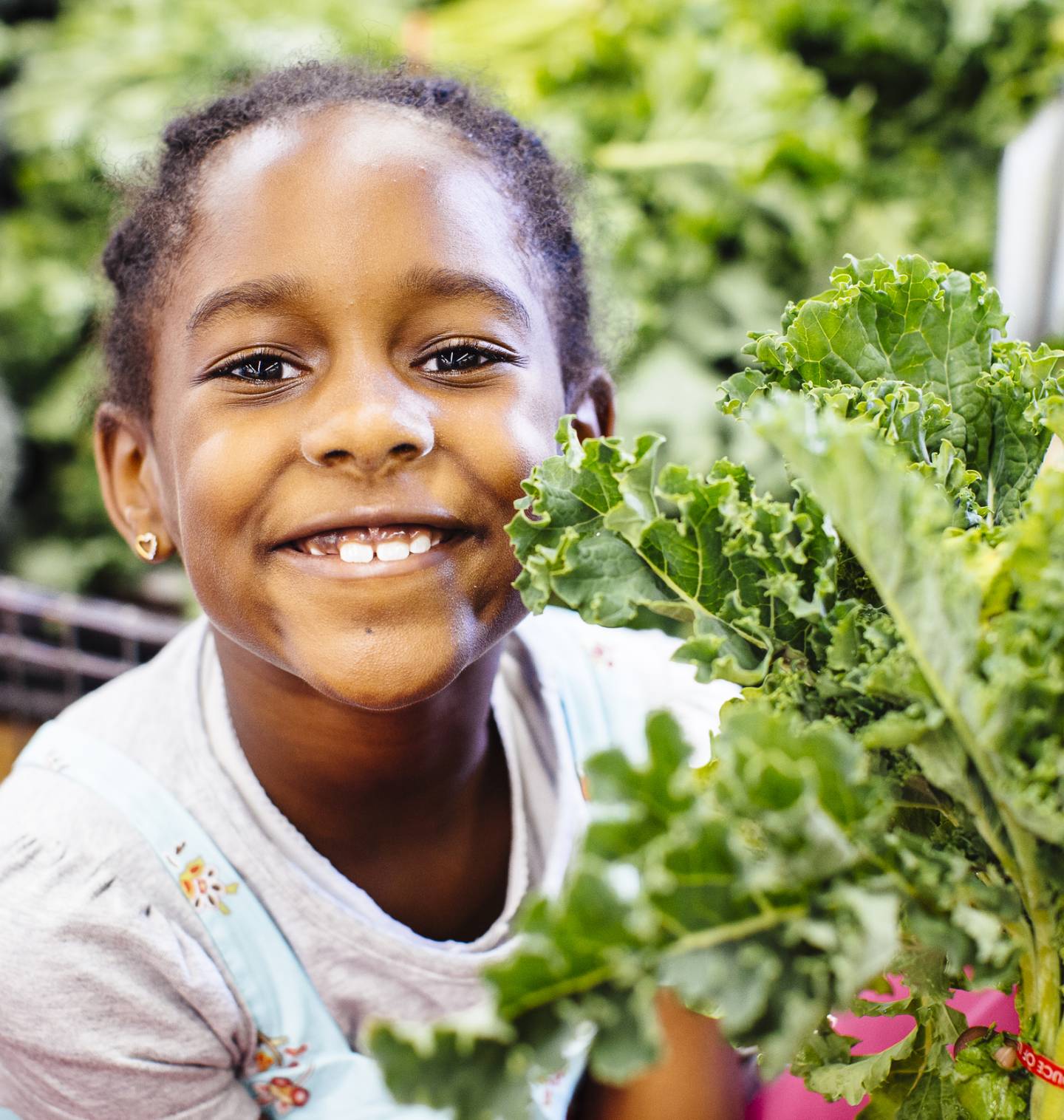 Young Black girl smiling in a shopping cart holding fresh greens