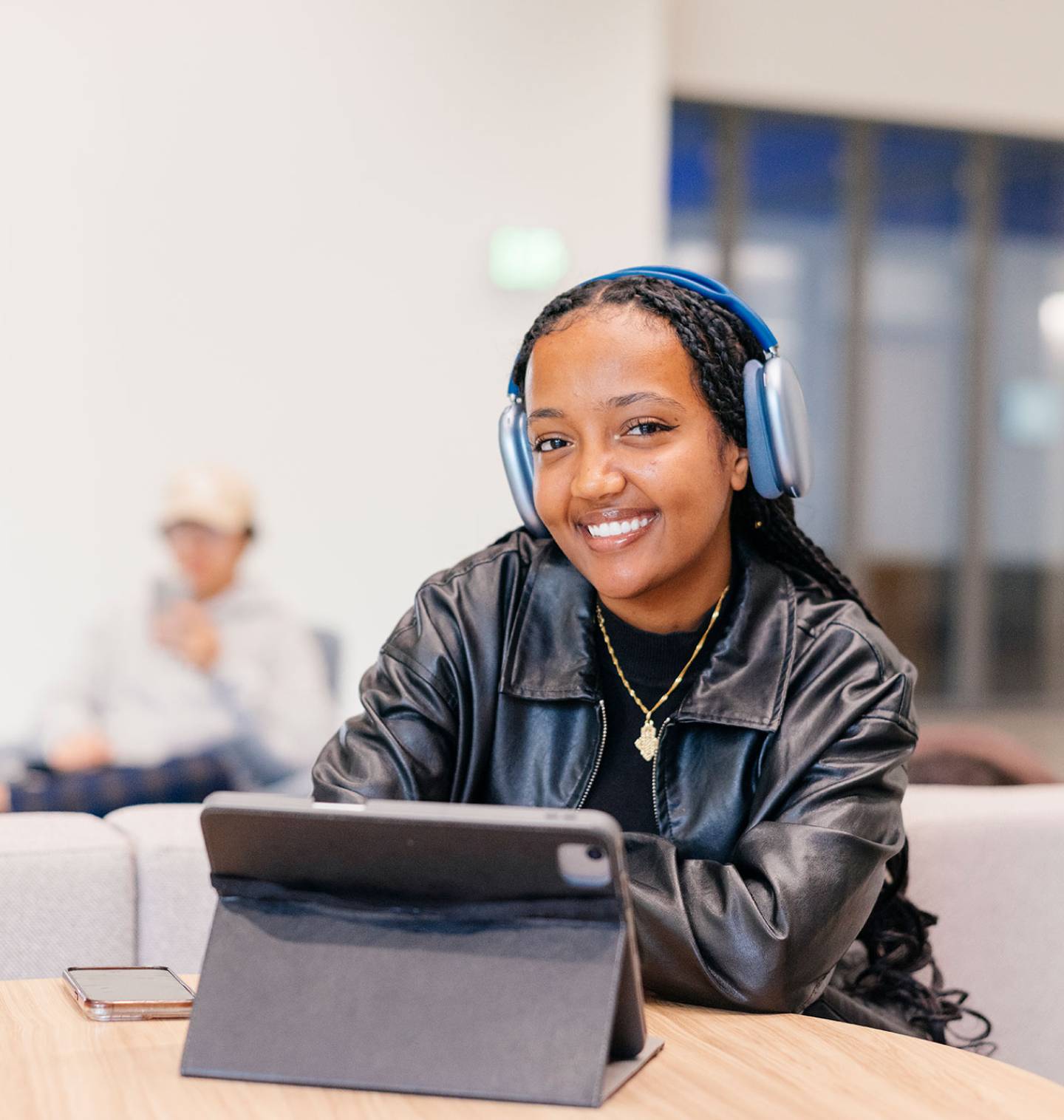 Student sitting at table smiling with headphones on and tablet on the table. 