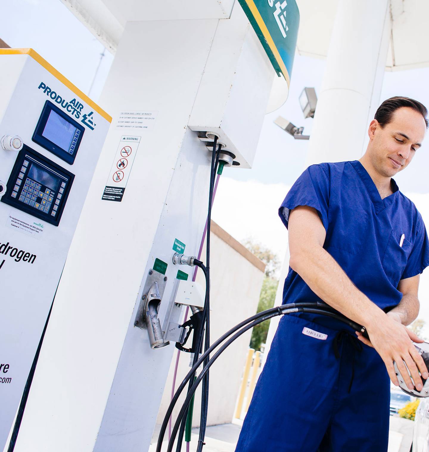 Person in scrubs using a hydrogen fuel pump to fuel a car.