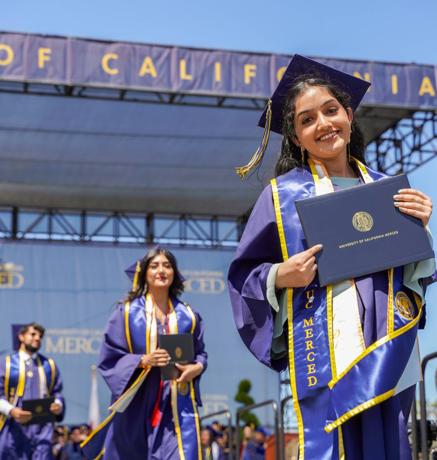 Students on stage at graduation with diplomas in hand