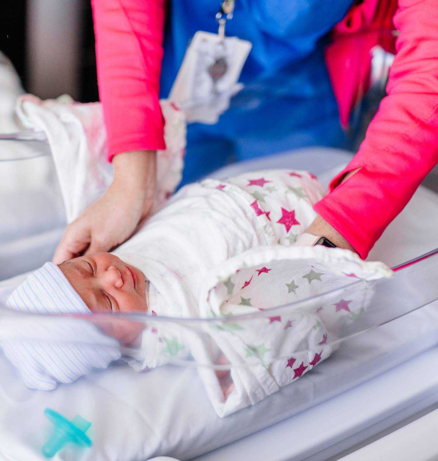 A nurse's arms reaching for a newborn baby in a hospital bassinet