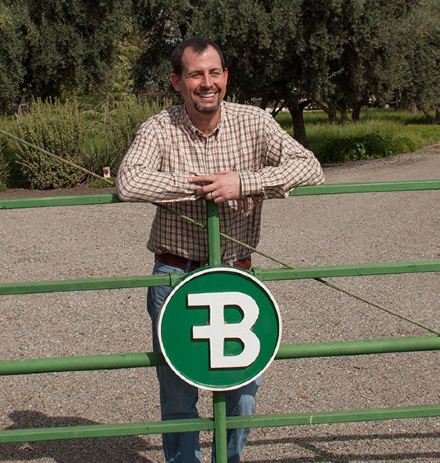 A man leans against a farm gate with a B on it