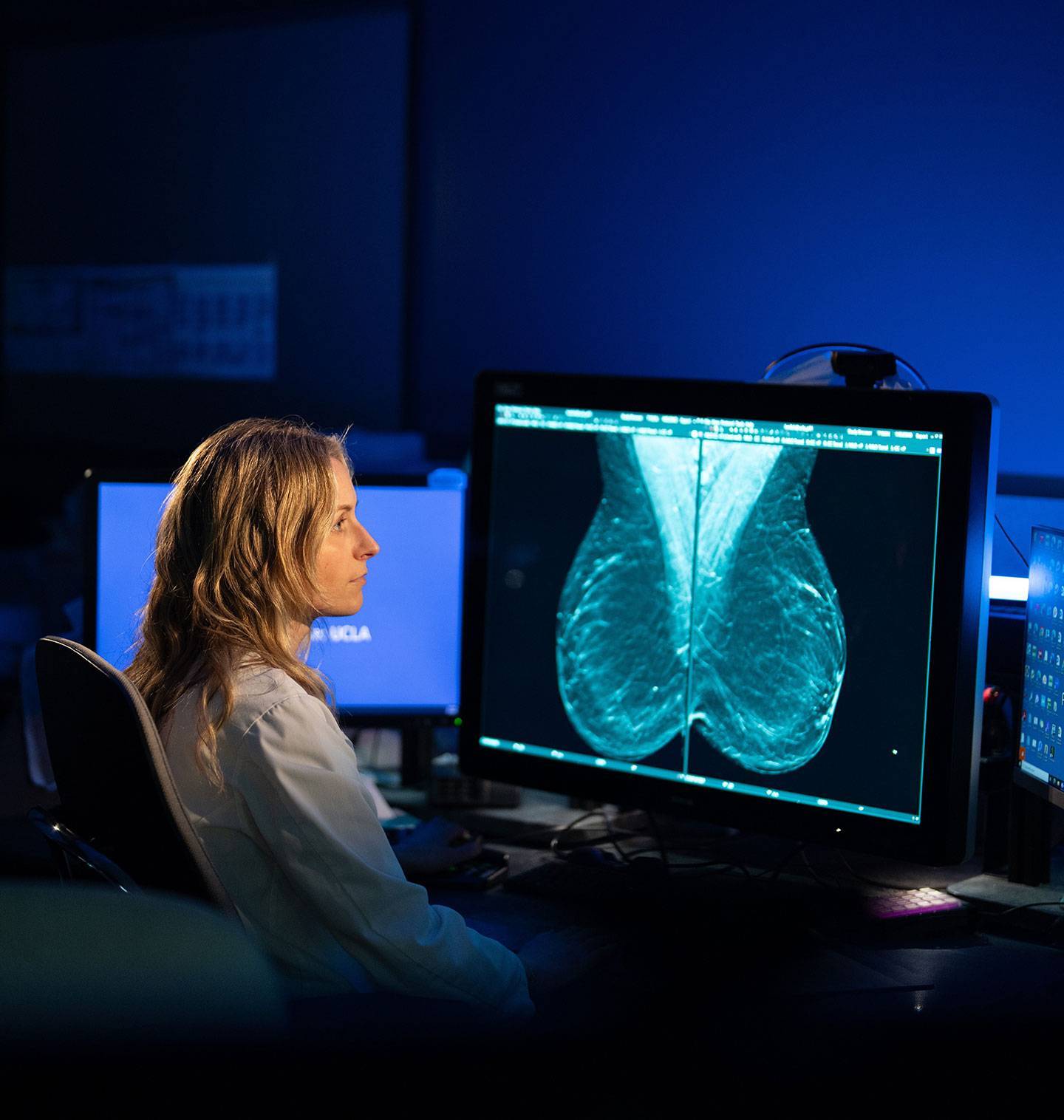 A radiologist studies an mammography image on a screen in a dark office