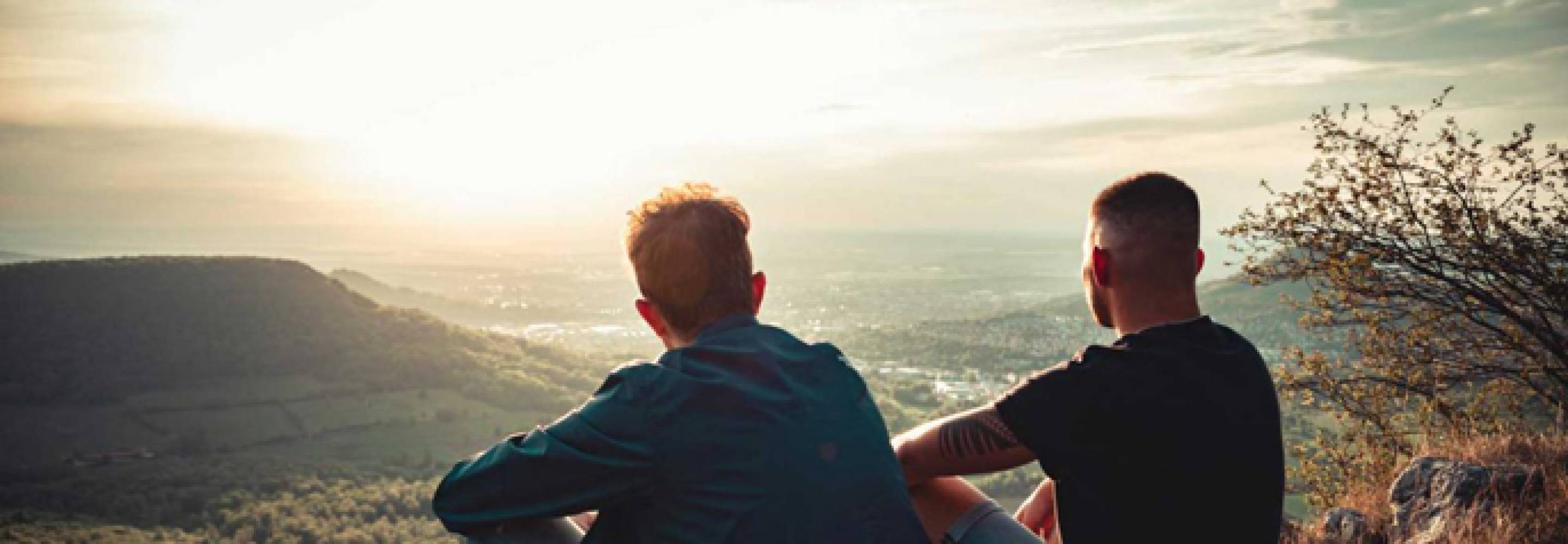 Two men stare down into a sunlit valley