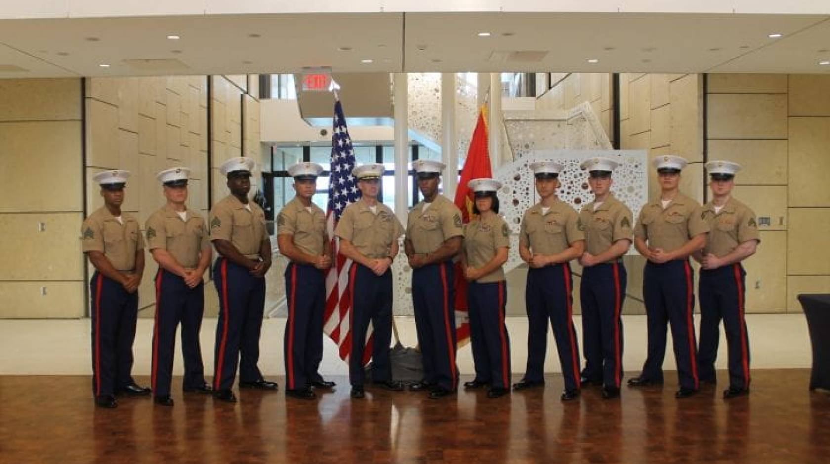 United States Marine Corps veteran and UCI sociology alumnus Andrew Truong ’23 (fourth from right), pictured with fellow service members, posing at ease in their uniforms in front of flags.