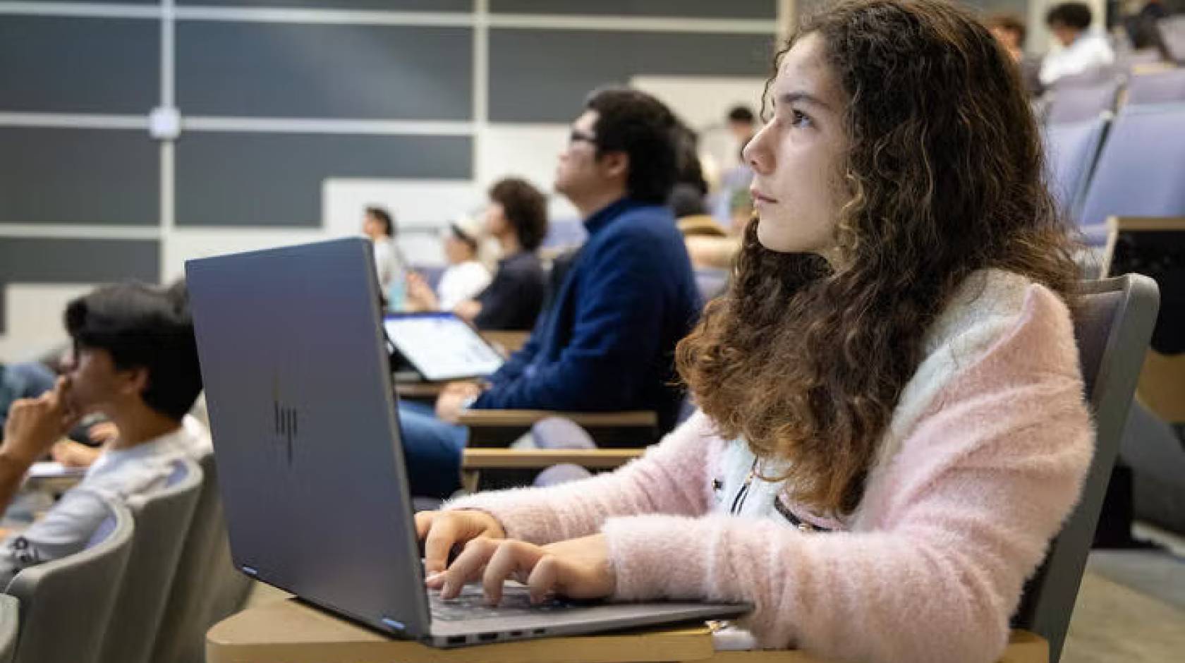 A pre-teen with long hair sits listening in a lecture hall