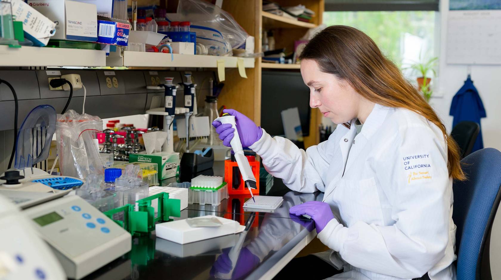 A student in a white lab coat with a pipette in the lab