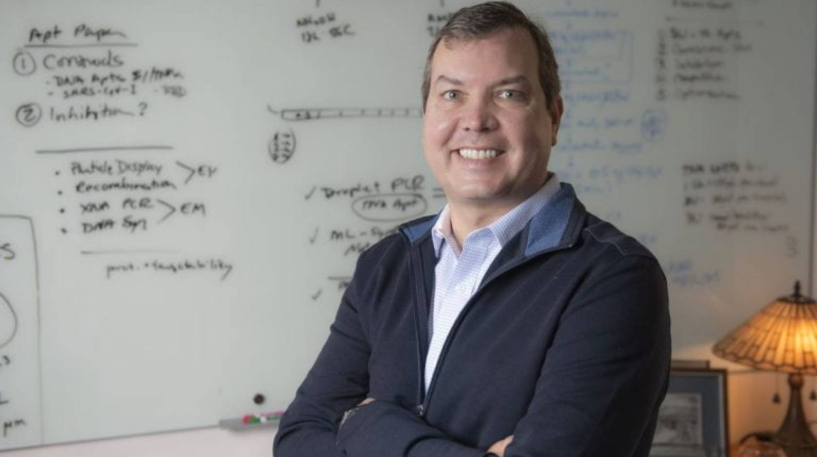 John Chaput, UCI professor of pharmaceutical sciences, stands smiling in front of a white board that is covered with notes.