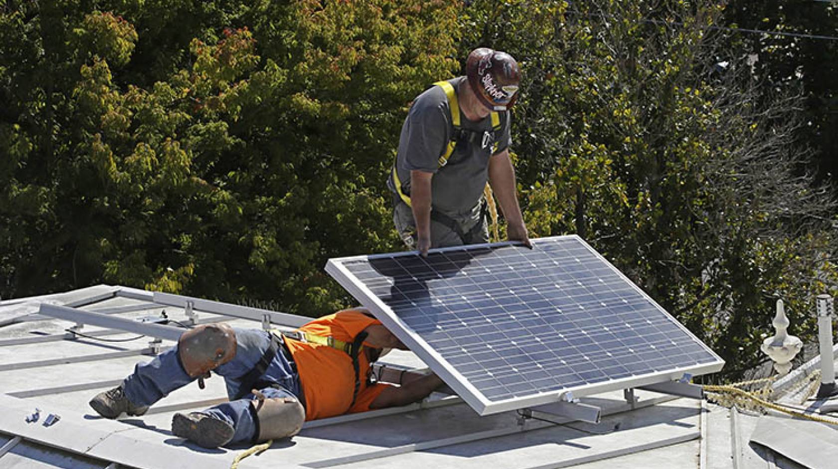 Workers install solar panels on a roof