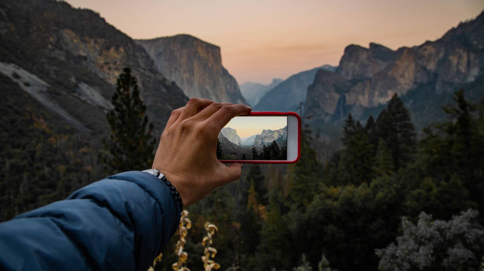 A hand holds a phone up to take a picture at sunset at Tunnel View in Yosemite National Park