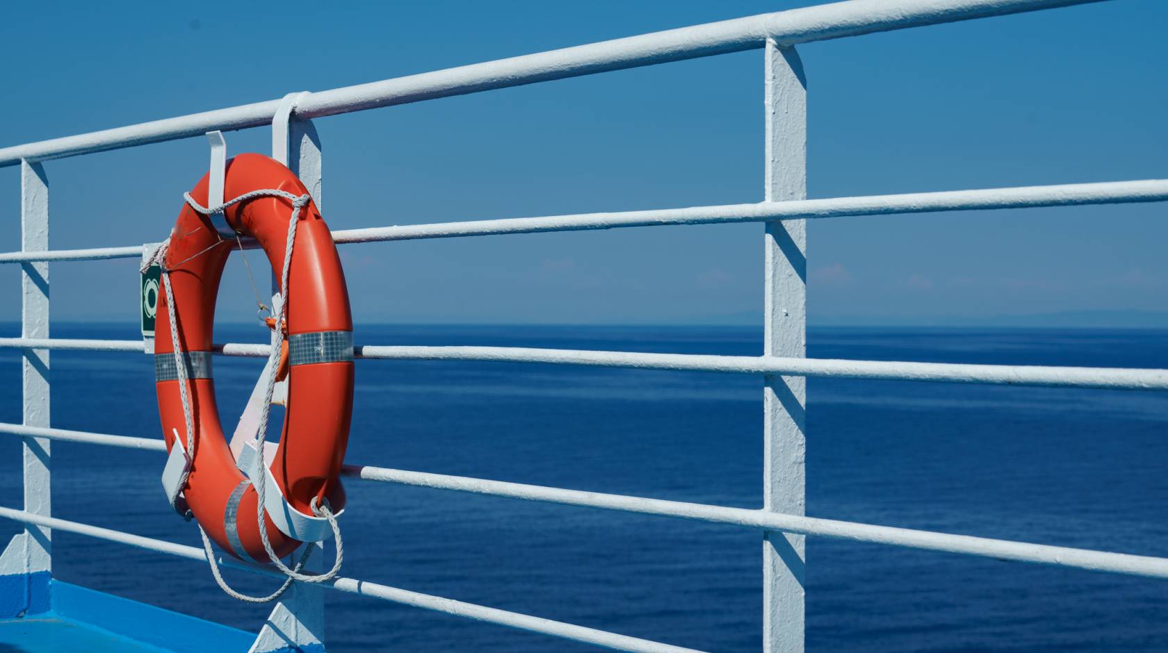 a red lifebuoy hangs on board a ferry cruise ship against the backdrop of a blue sea and a cloudless sky