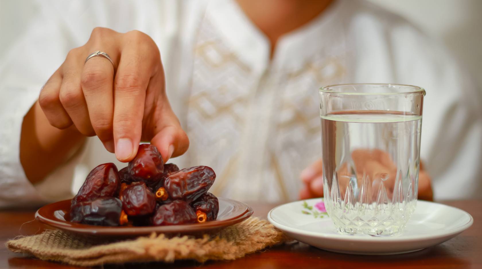 A plate full of dates and a glass of water, with a hand reaching for a date