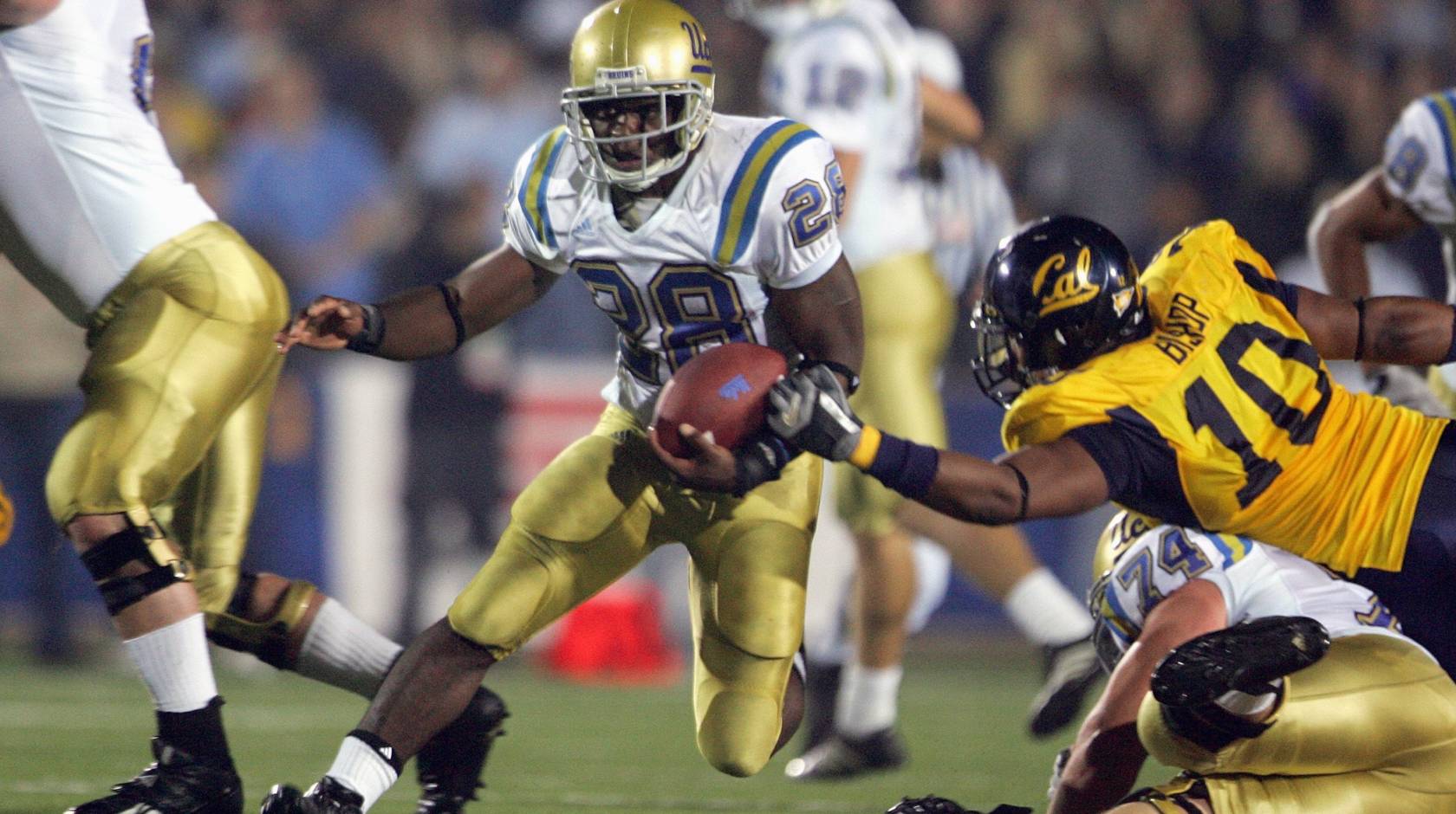 A UCLA football player carries the ball past a diving Cal player while another UCLA player blocks to his right