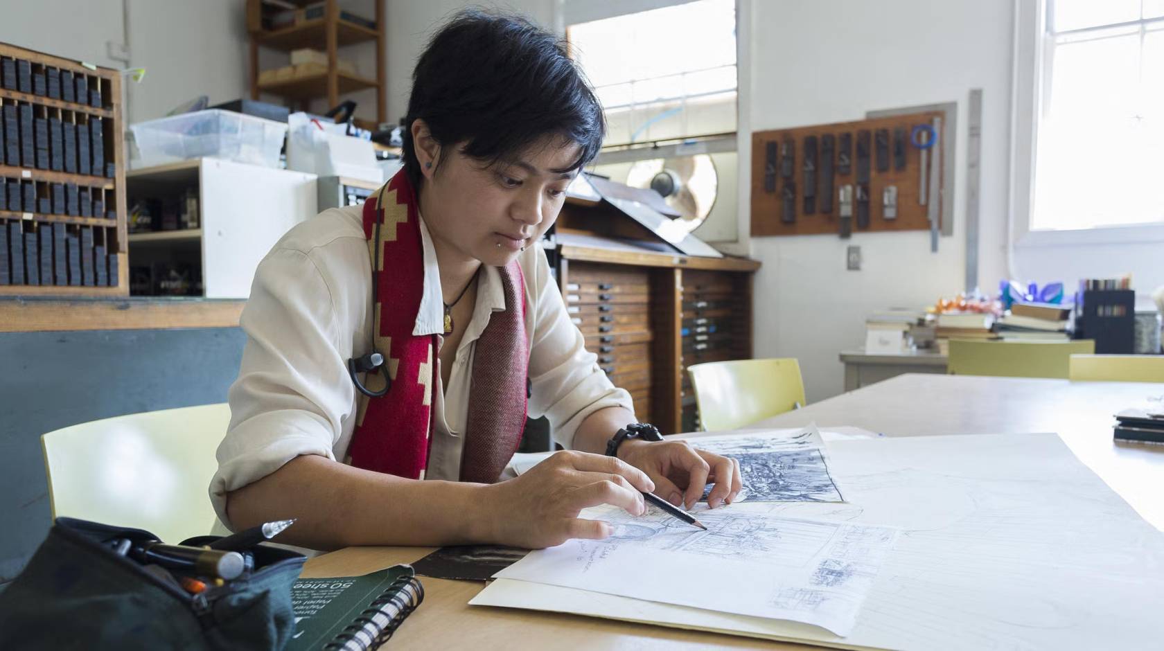A student in an art studio holds a pencil over a sketchbook