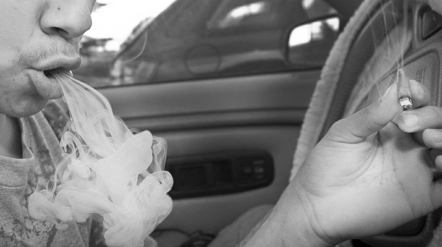 A man behind the wheel of a car exhales a big puff of smoke