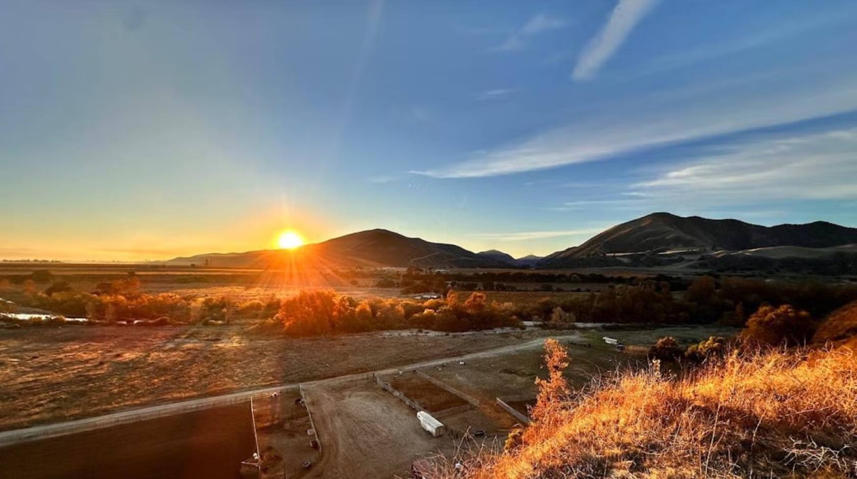 Sunrise over rolling hills, casting warm light on the landscape and clear blue sky.