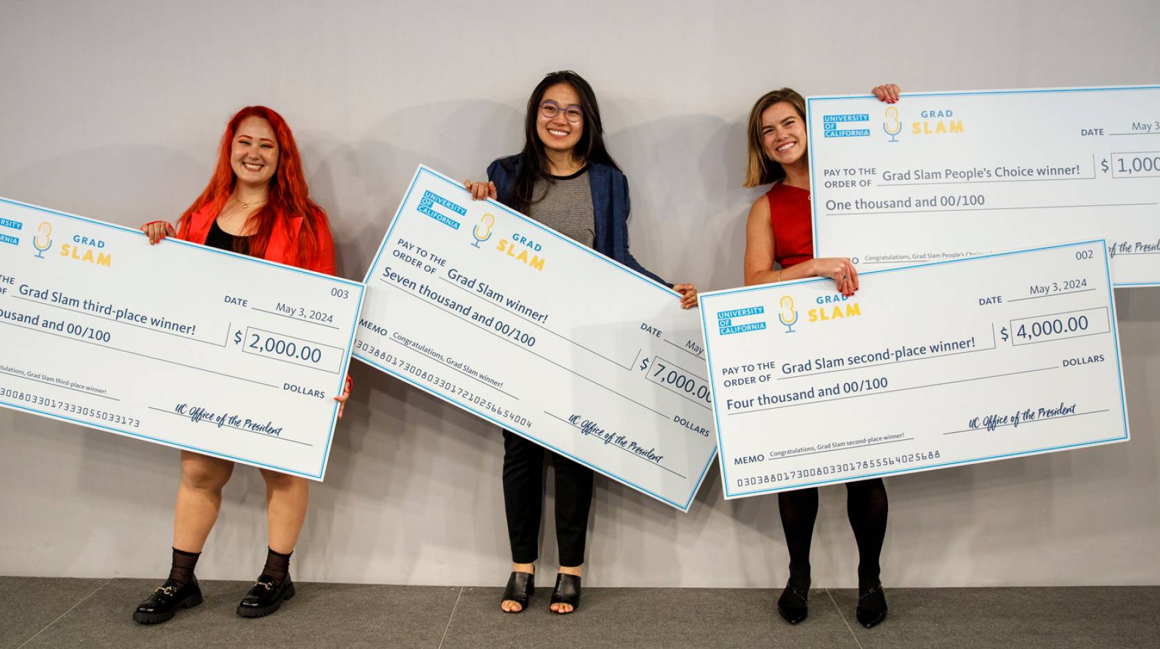 Three people standing holding giant checks