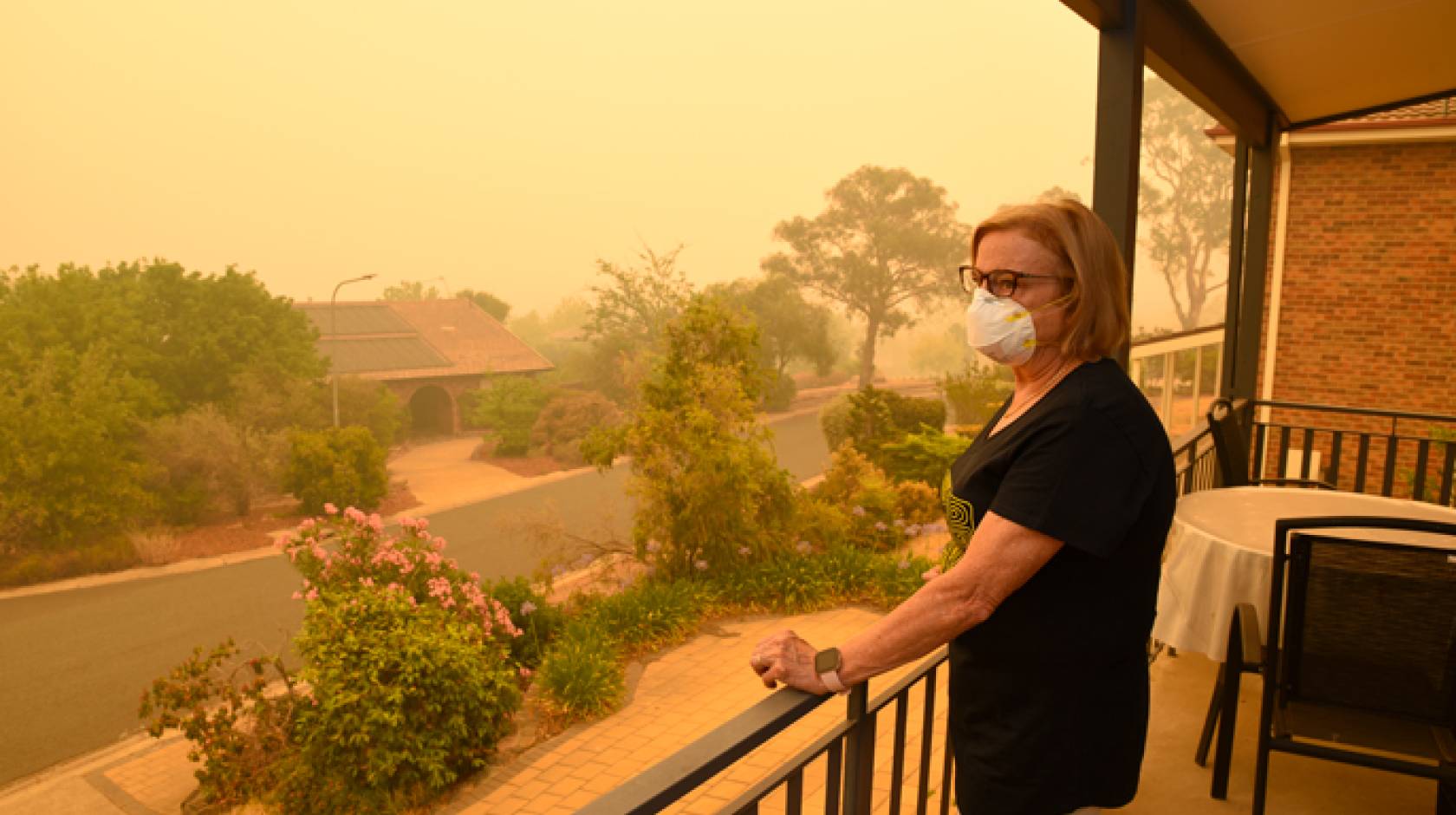 A woman in a mask stares out from her porch at orange air