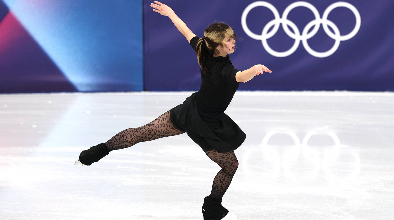 A figure-skating woman woman stretches her arms and back leg while practicing on the ice