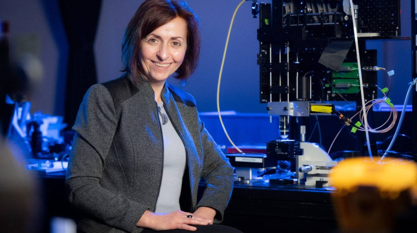 A woman smiles in front of a piece of equipment in a lab