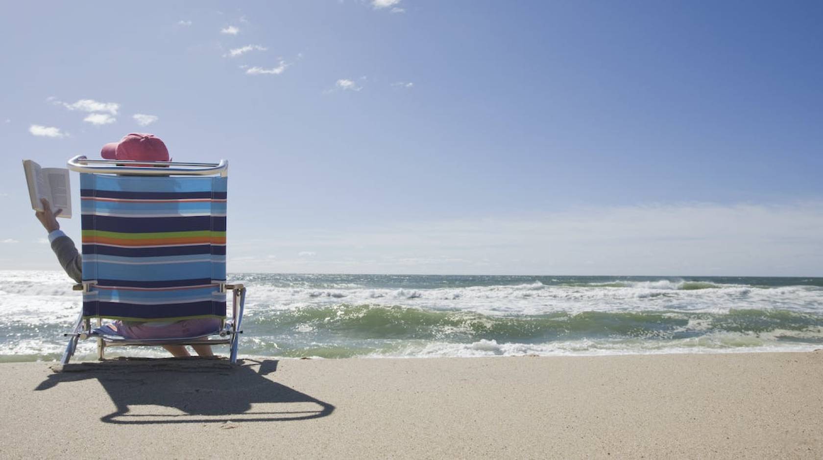 Person reading on the beach, photographed from the back with the ocean in front