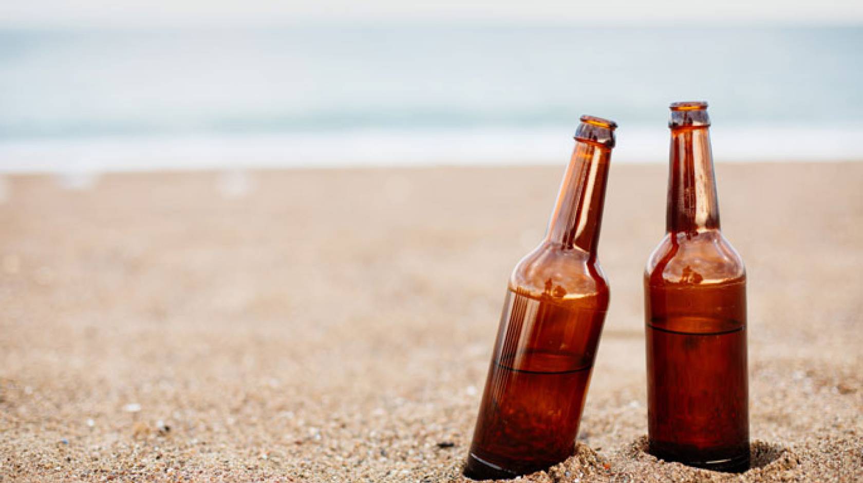 Two half-full beers on a sandy beach
