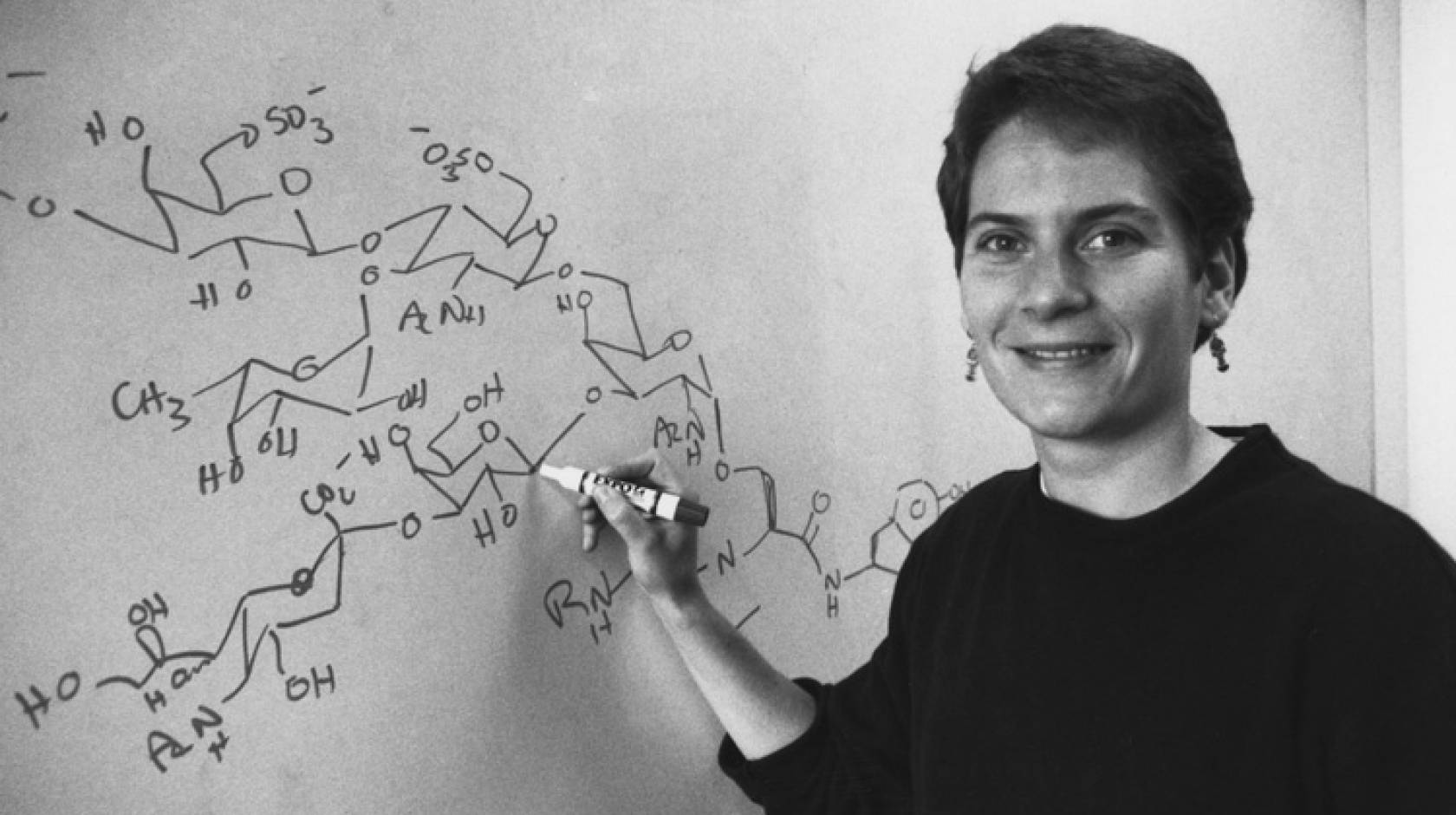 Black and white photo of Carolyn Bertozzi at a chalkboard