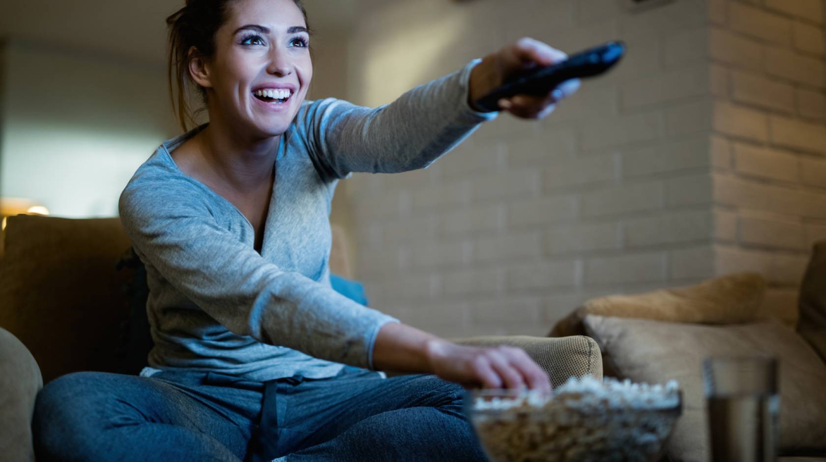 A young woman smiling holding a remote and eating popcorn