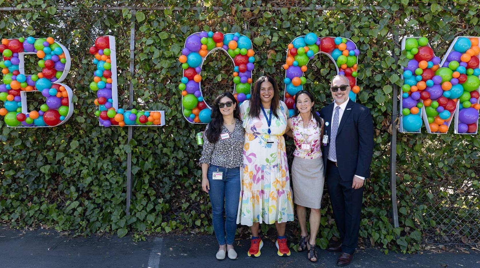 Four people outdoors in front of a sign made of balloons that says 'Bloom'