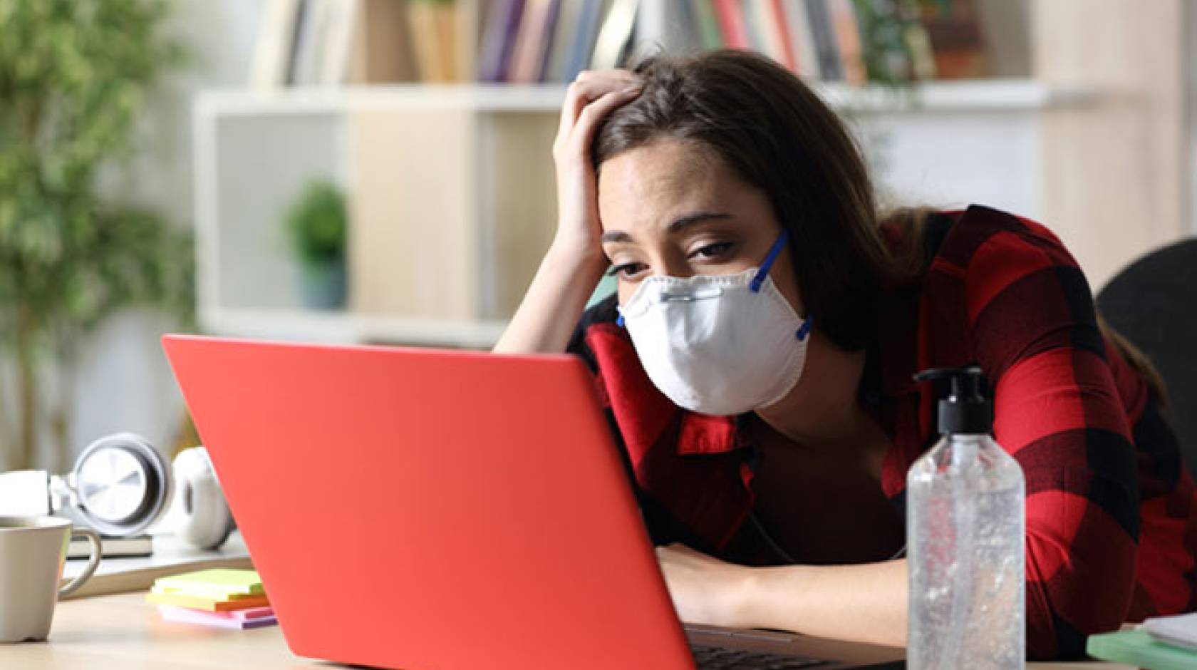 Student in mask looks at computer, bored