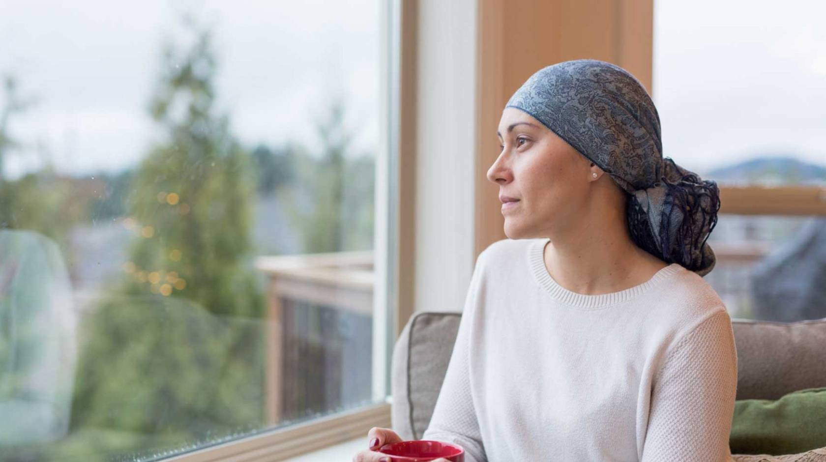 Woman recovering from breast cancer wearing a scarf on her head stares out the window