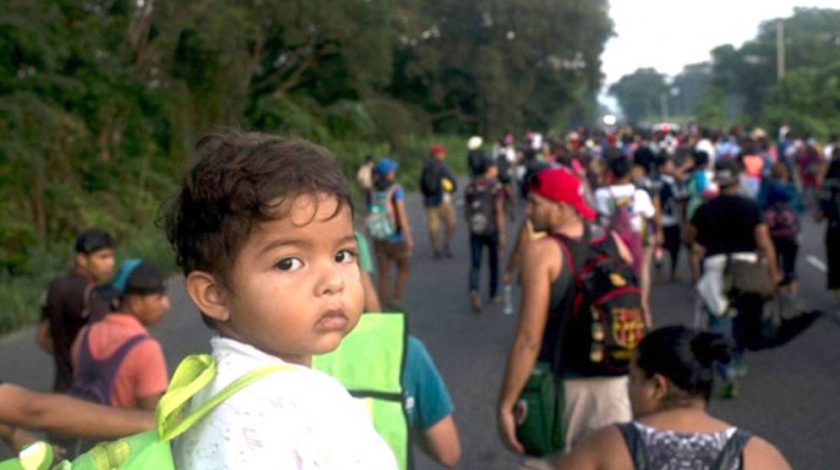 A child looks at the camera from among a group of migrants