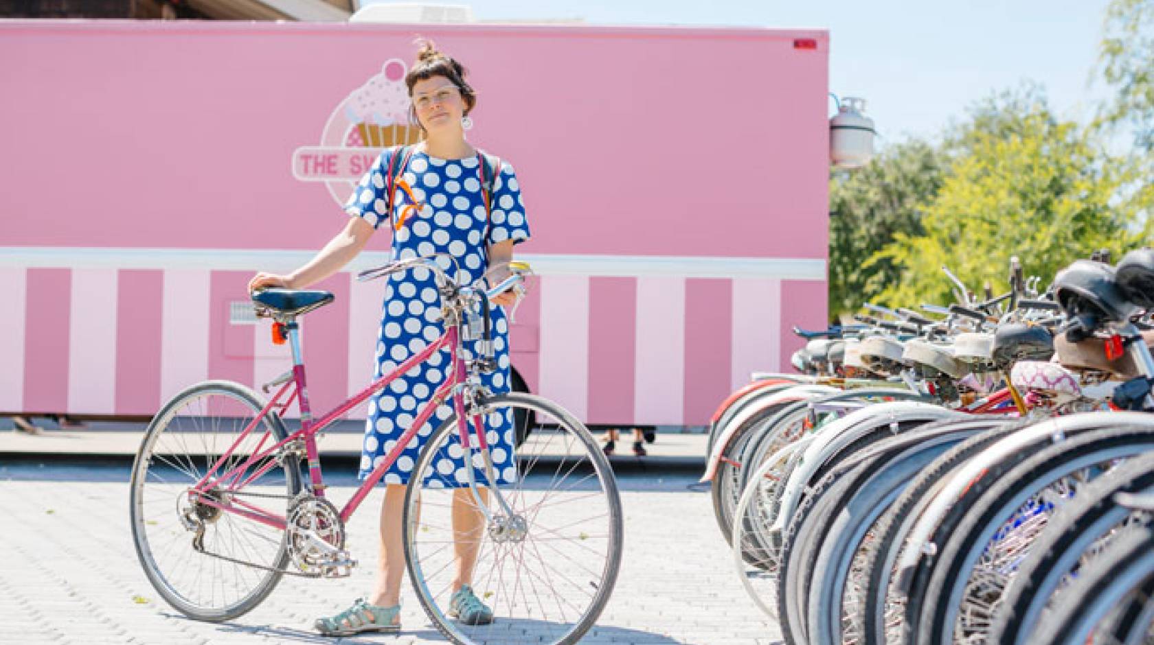 Woman in polka dot dress standing with bike at bike rack