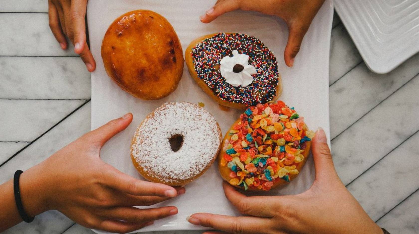 Multiple hands reaching for donuts