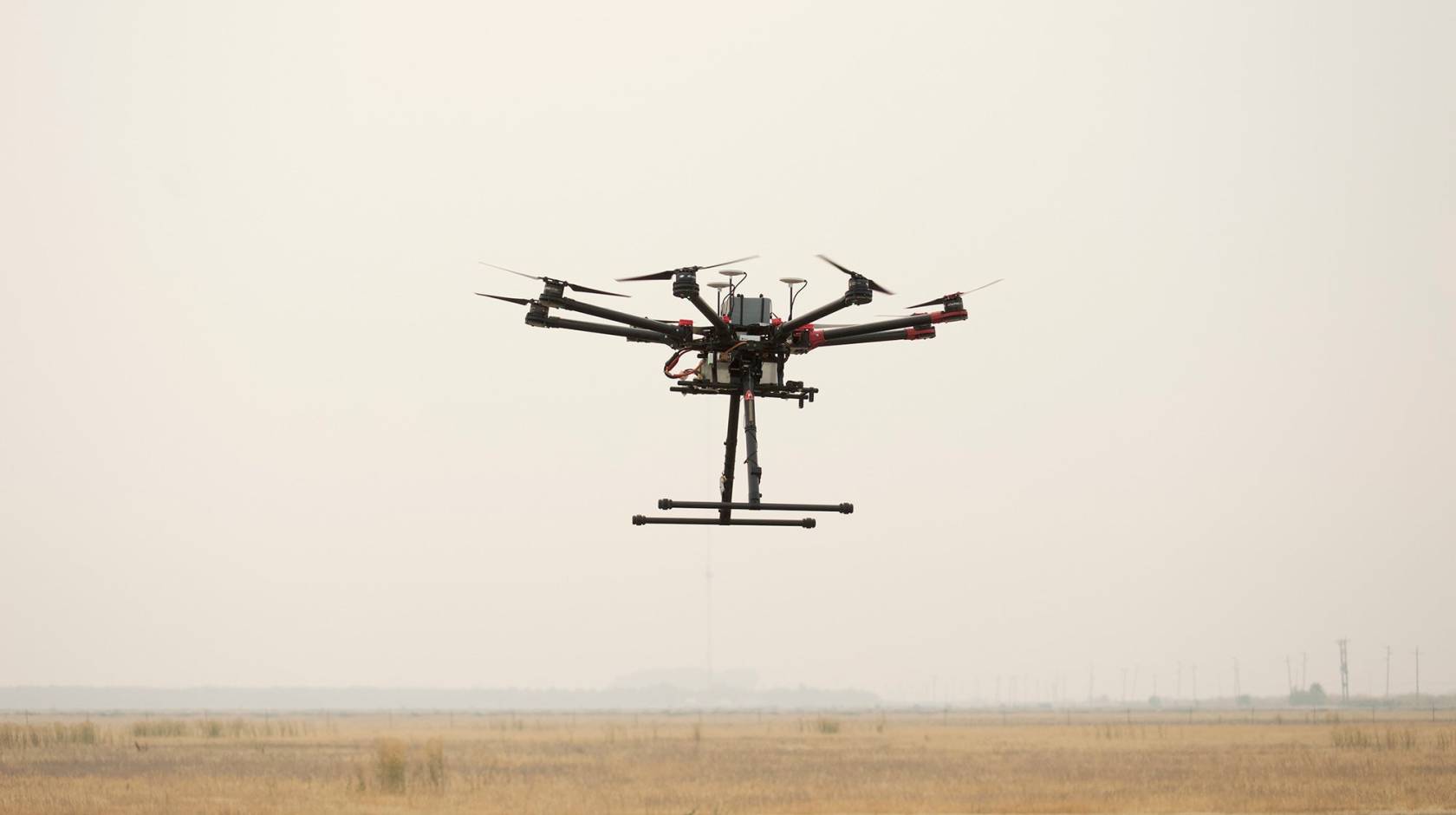 A drone hovers in smoky air over a field