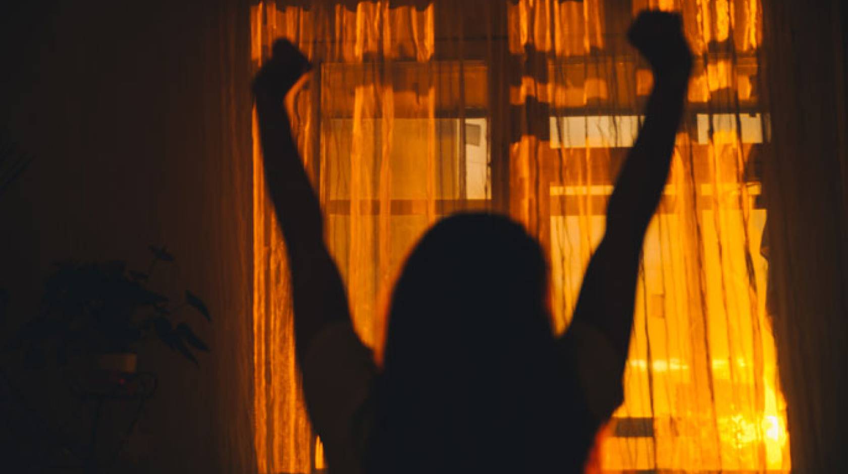 Woman stretching in a room behind curtains that show the dawn