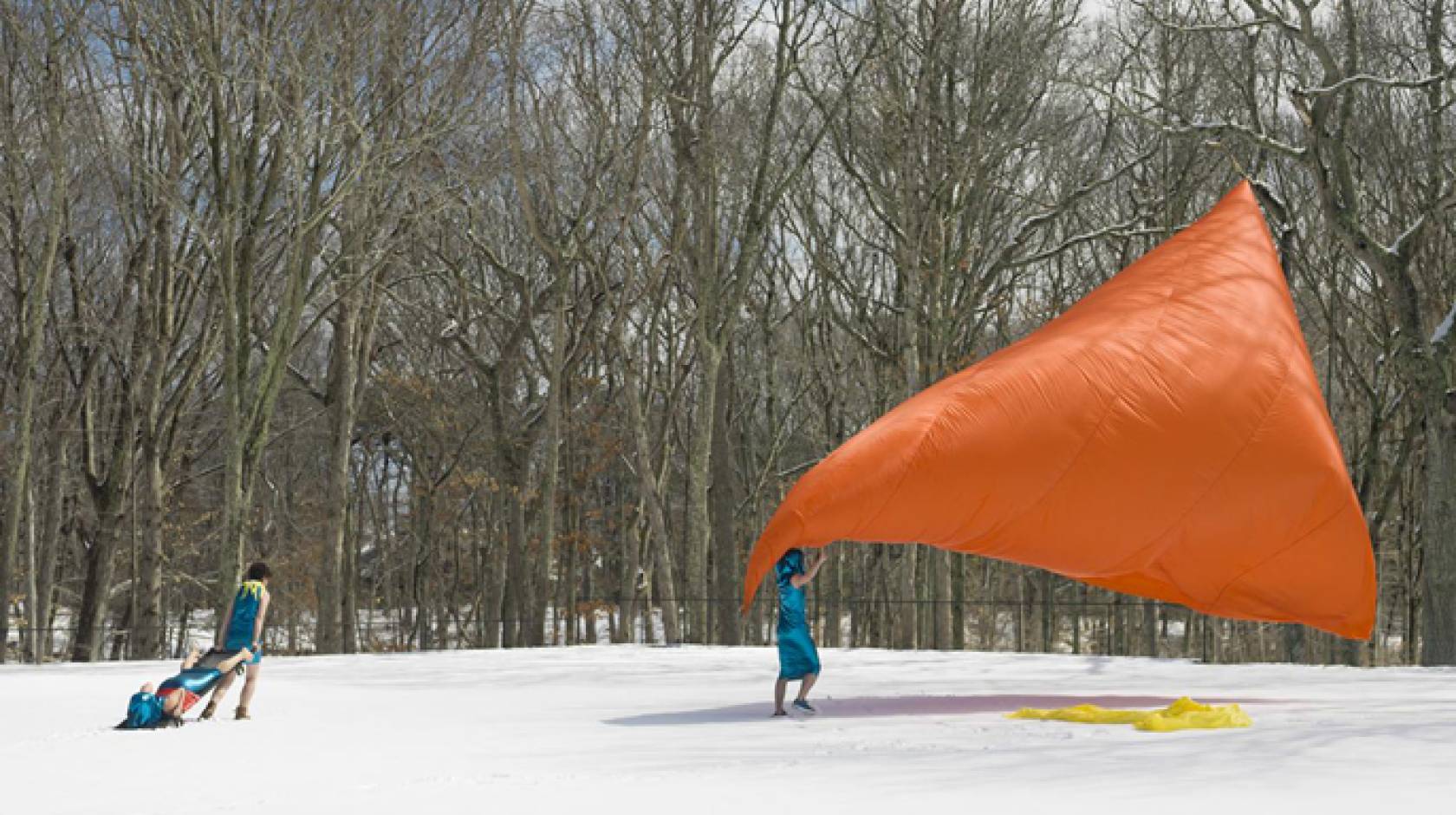 Three people performing with a giant orange sheet outside in the snow