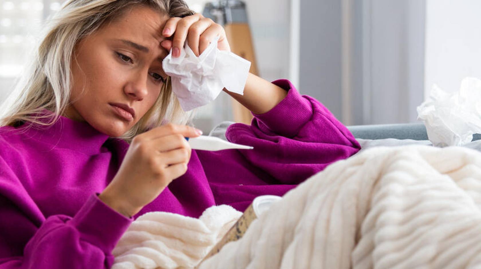 Woman sitting on a couch looking a thermometer