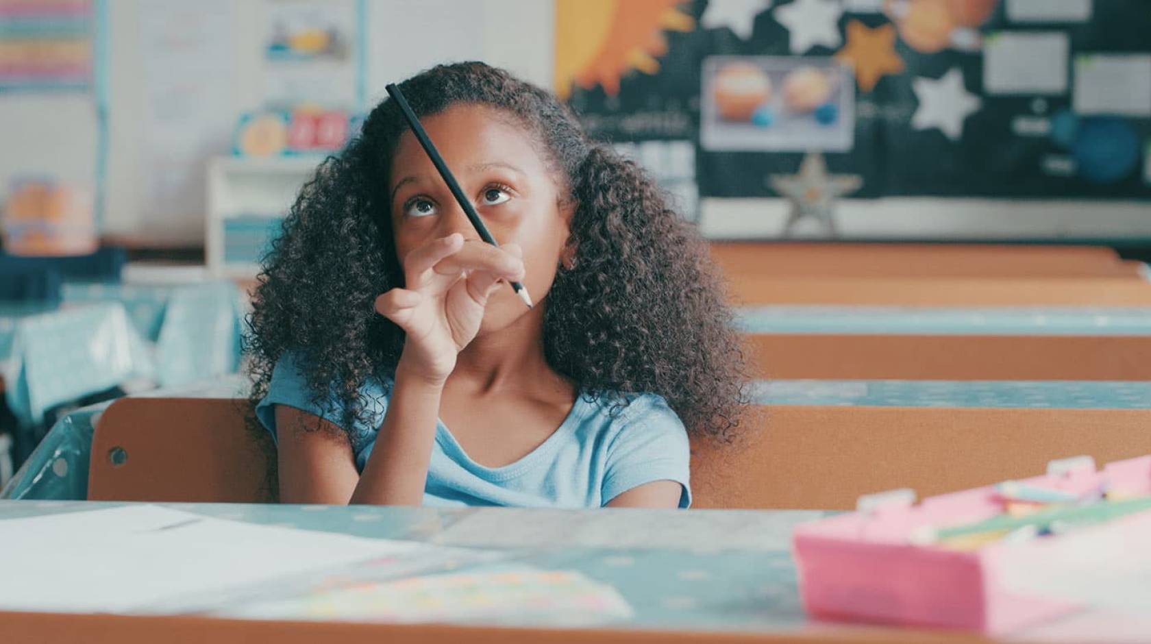 Young Black girl in classroom playing with her pencil, bored