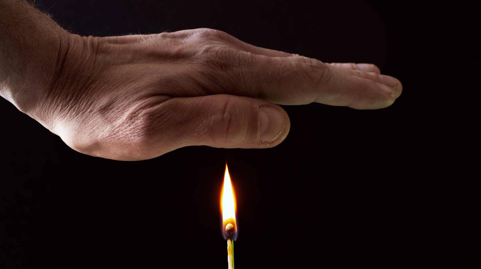 A hand held over a flame from a match